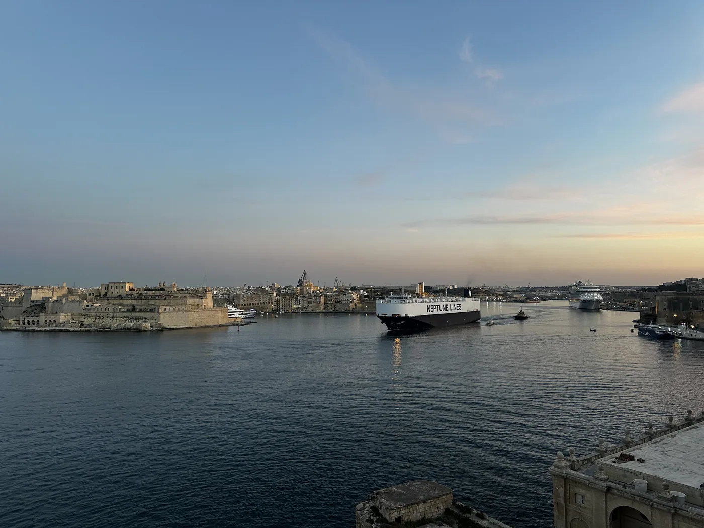 The Grand Harbour at dusk, with a ferry on the water and the fortified shore in the distance